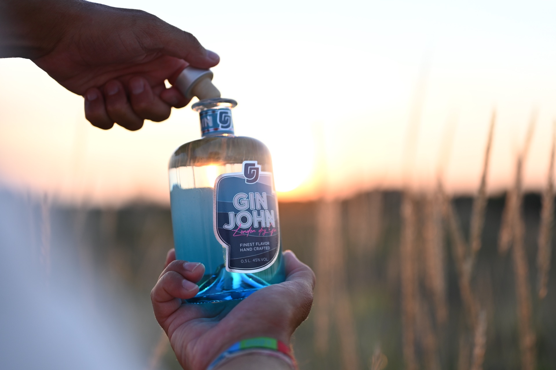 Gin John wird in einem Kornfeld bei Sonnenuntergang von zwei Händen weitergereicht – ein goldener Moment